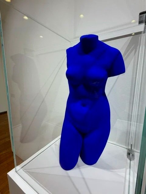 A blue female mannequin torso on display in a glass case, without a head or arms.