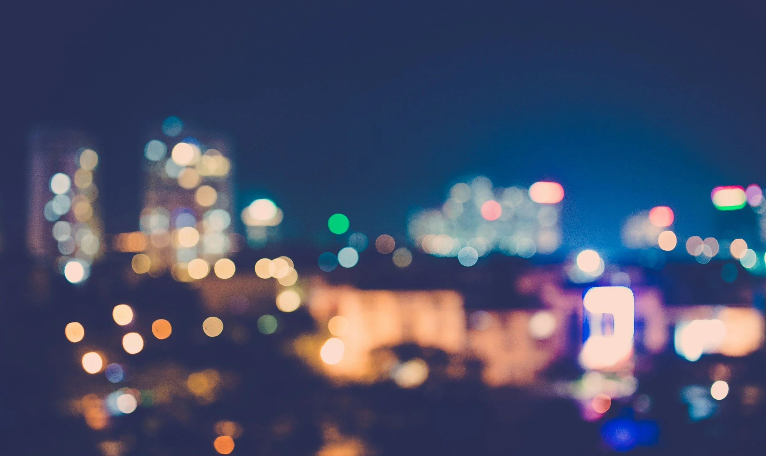 Blurred cityscape at night with colorful bokeh lights and dark sky.