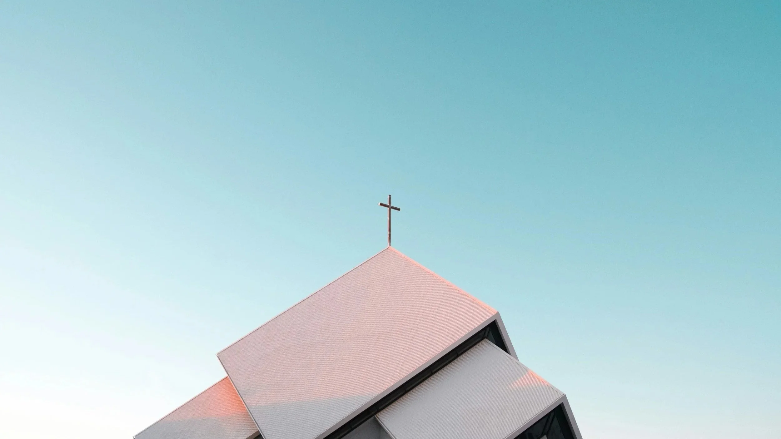 The top of a modern church building with a cross on its steeple, set against a clear blue sky.