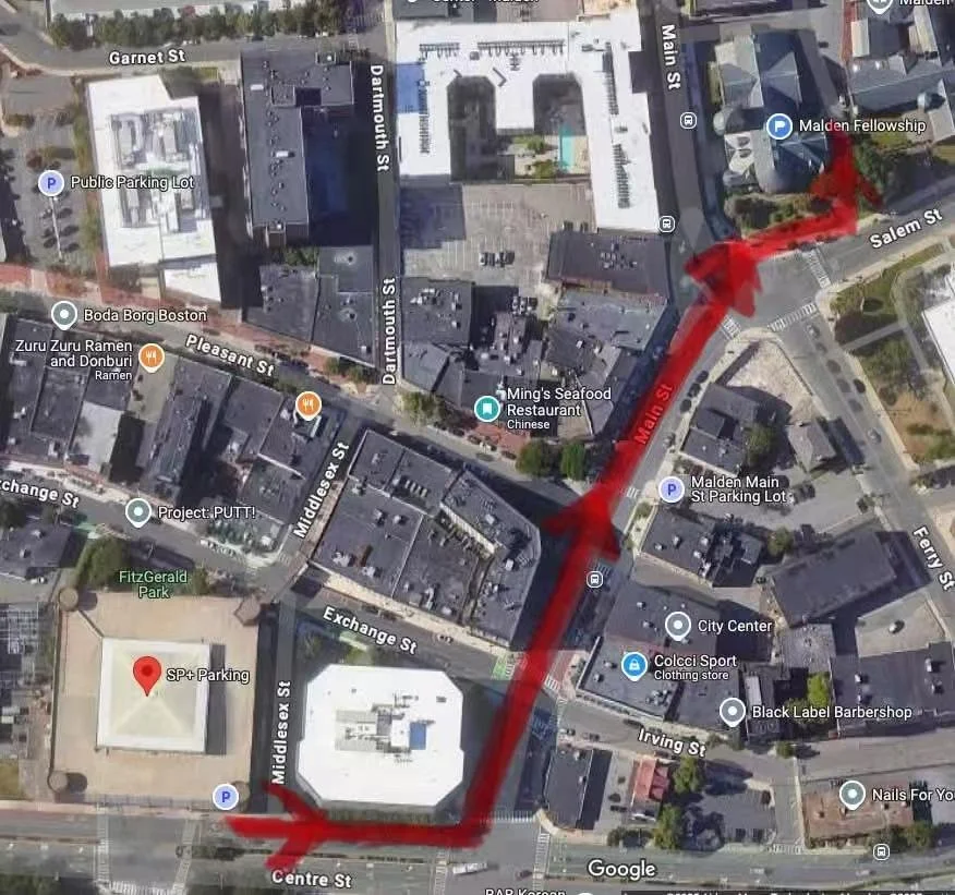 A satellite map showing a route marked in red through streets in an urban area, passing by parking lots, restaurants, businesses, and parks.