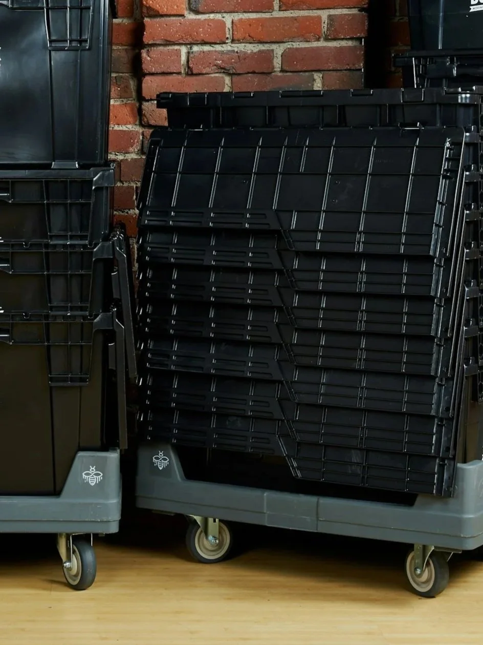 Stacked black plastic storage bins on a gray rolling cart in front of a brick wall.