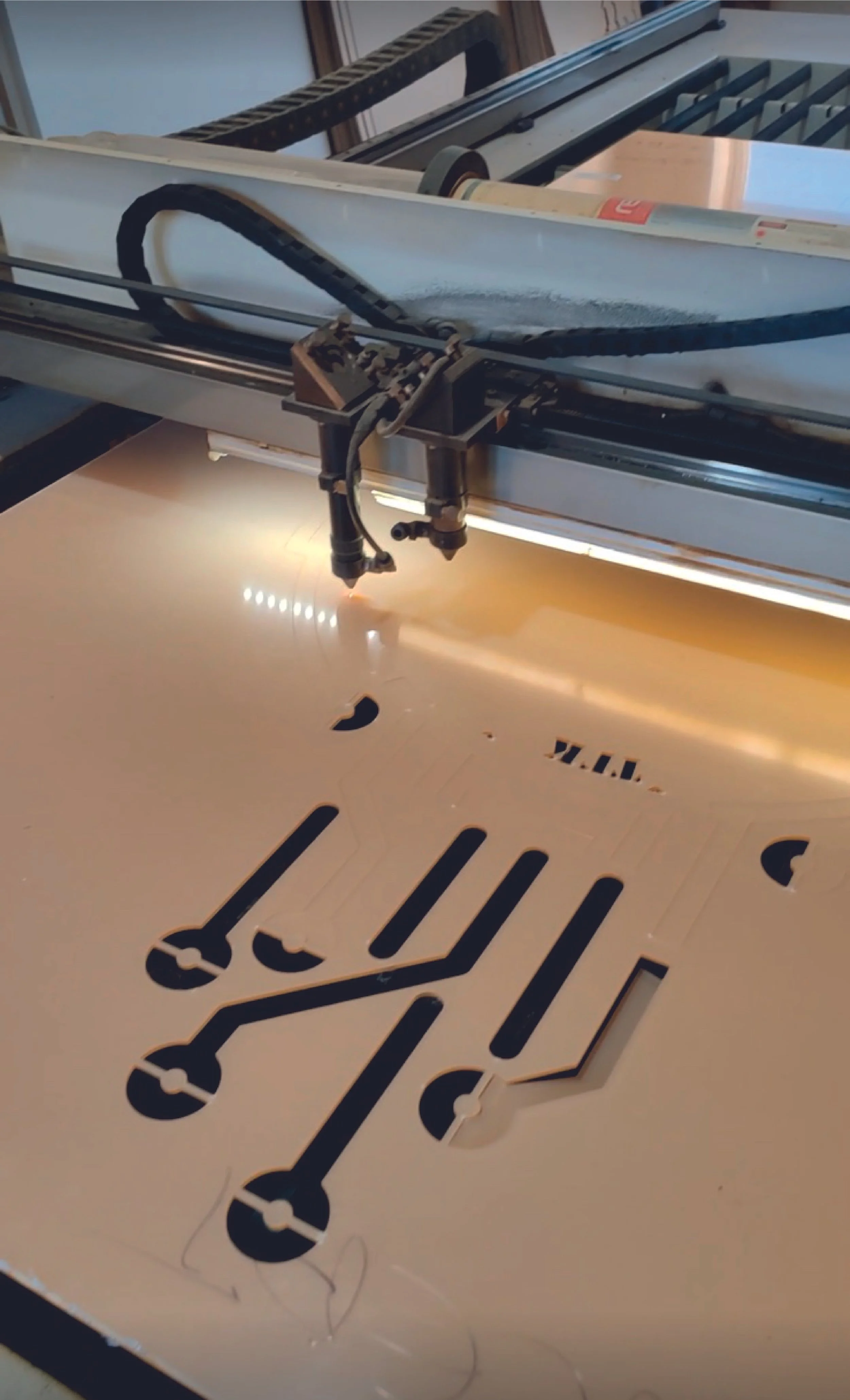 Close-up of a laser cutting machine shaping a sheet of metal with black cut-out patterns.