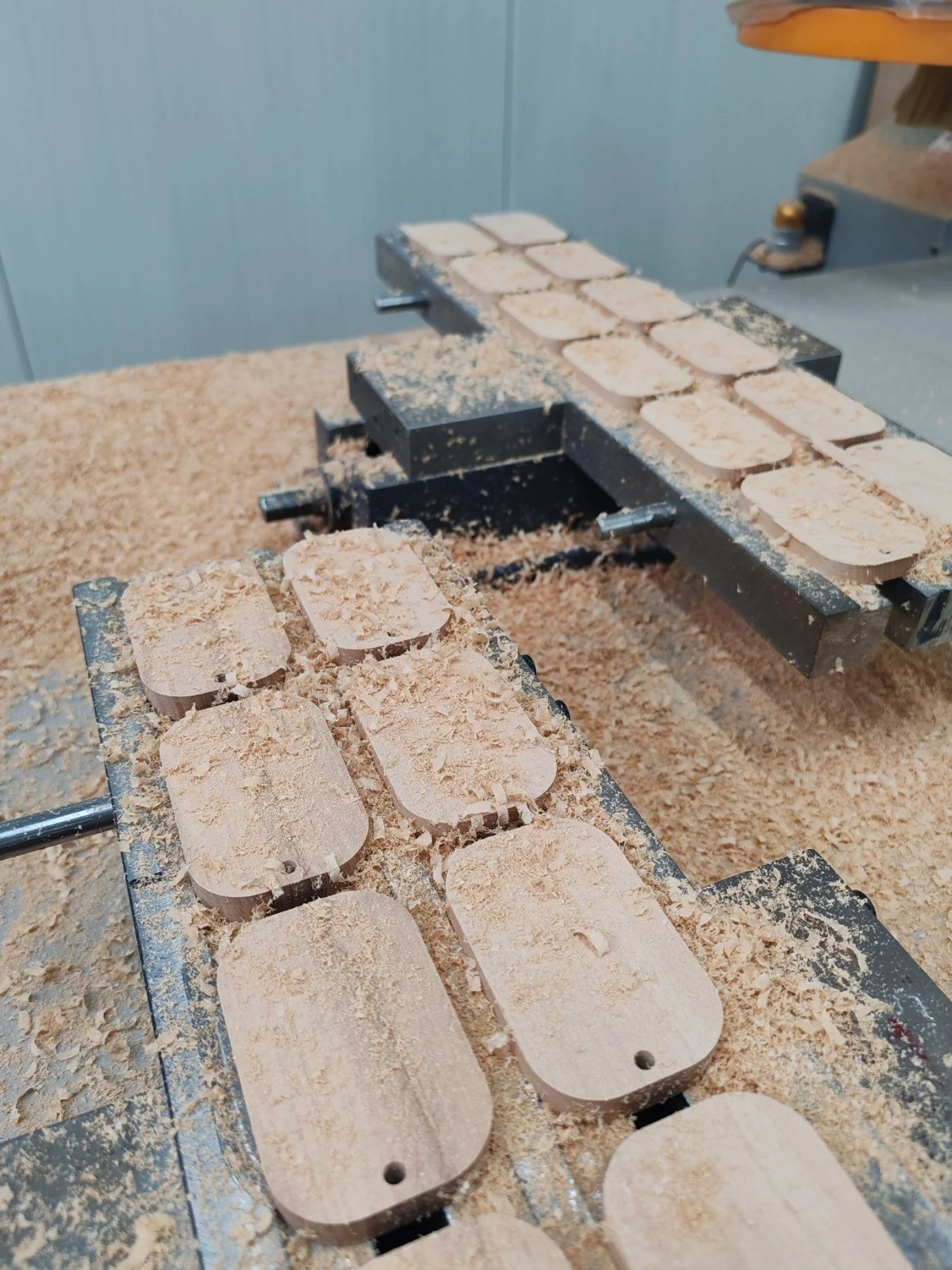 Wooden blocks with holes being carved on a machine, surrounded by sawdust in a woodworking shop.