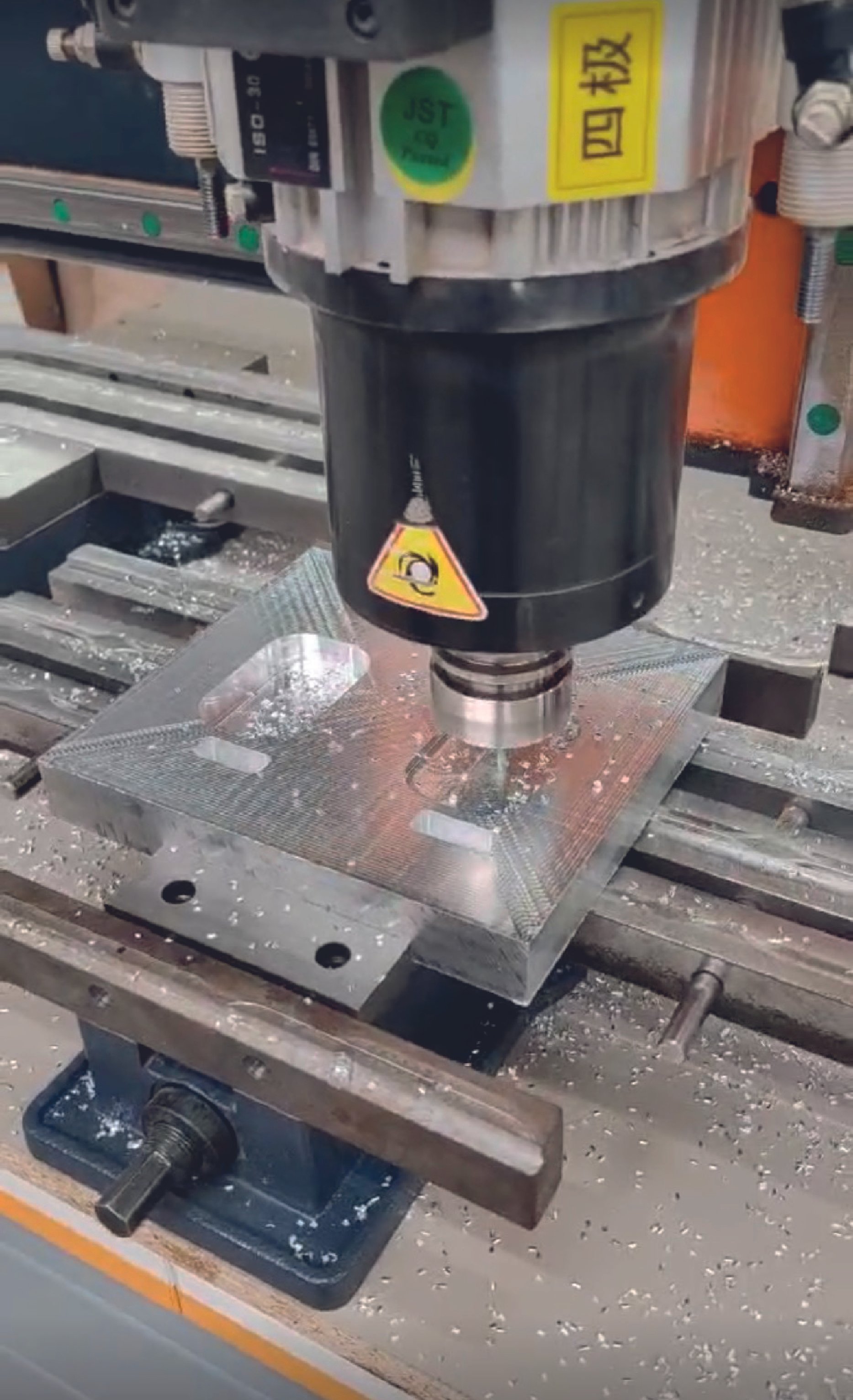 Close-up of a CNC machine milling a metal workpiece, with metal shavings on the machine bed and a warning label on the machine spindle.