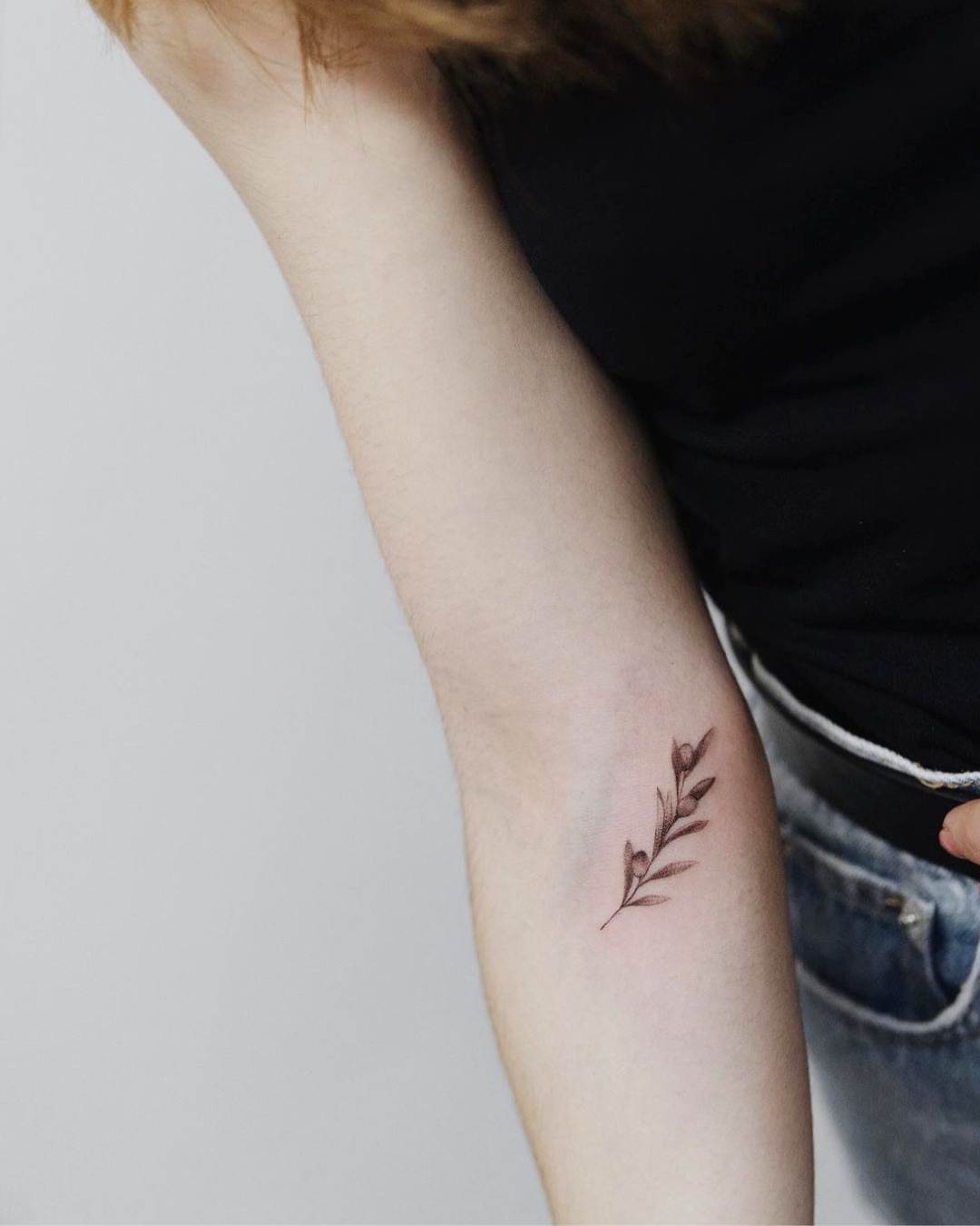 Tatuaje Fine Line botánico de rama con hojas olivo realizado por Manuela Medina