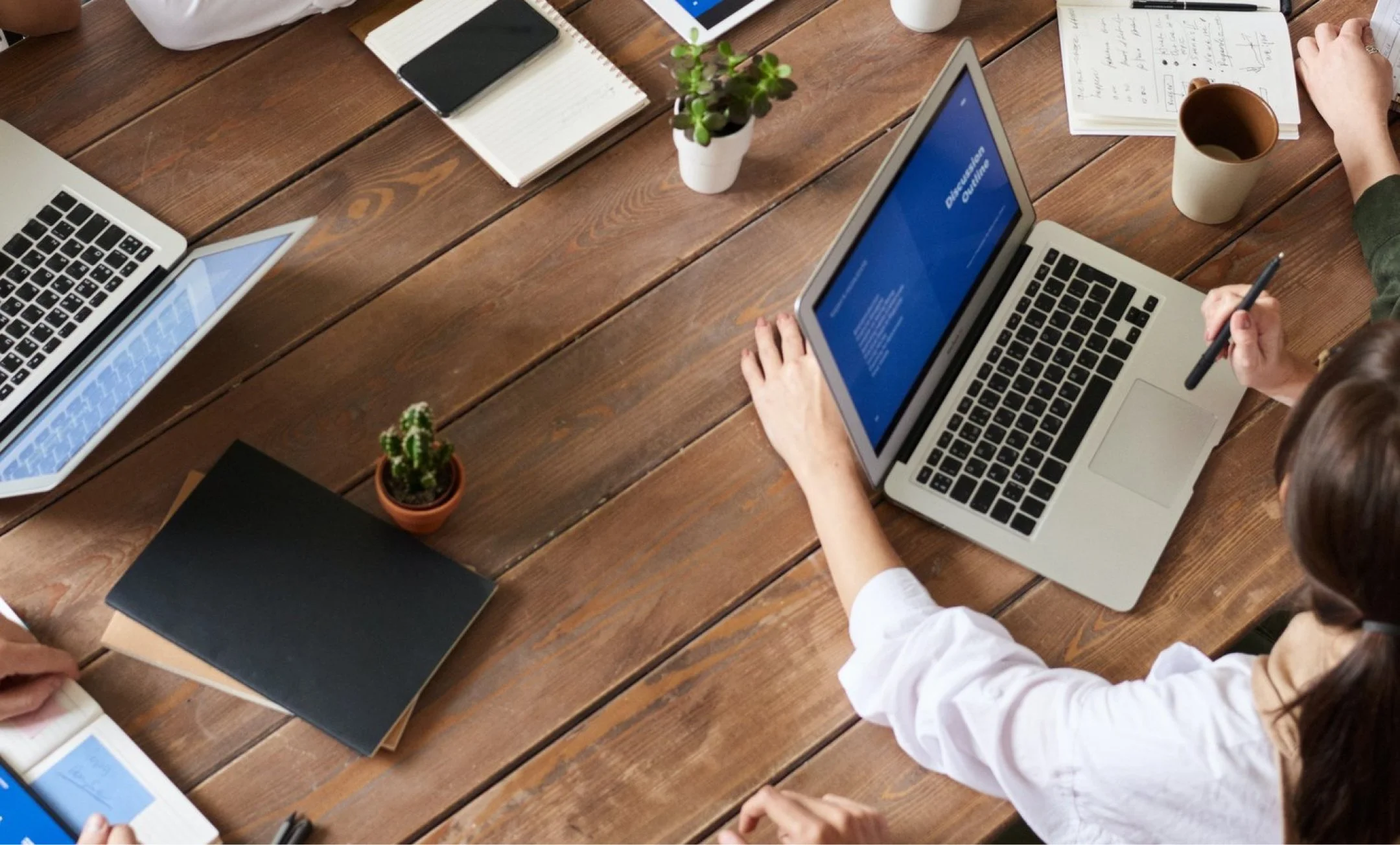 wooden table with a person who is using their laptop in a middle of a meeting