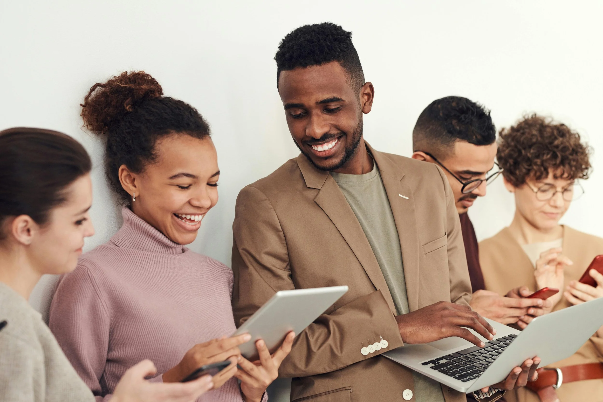 a group of 5 co-workers standing against a wall in the office using their gadgets