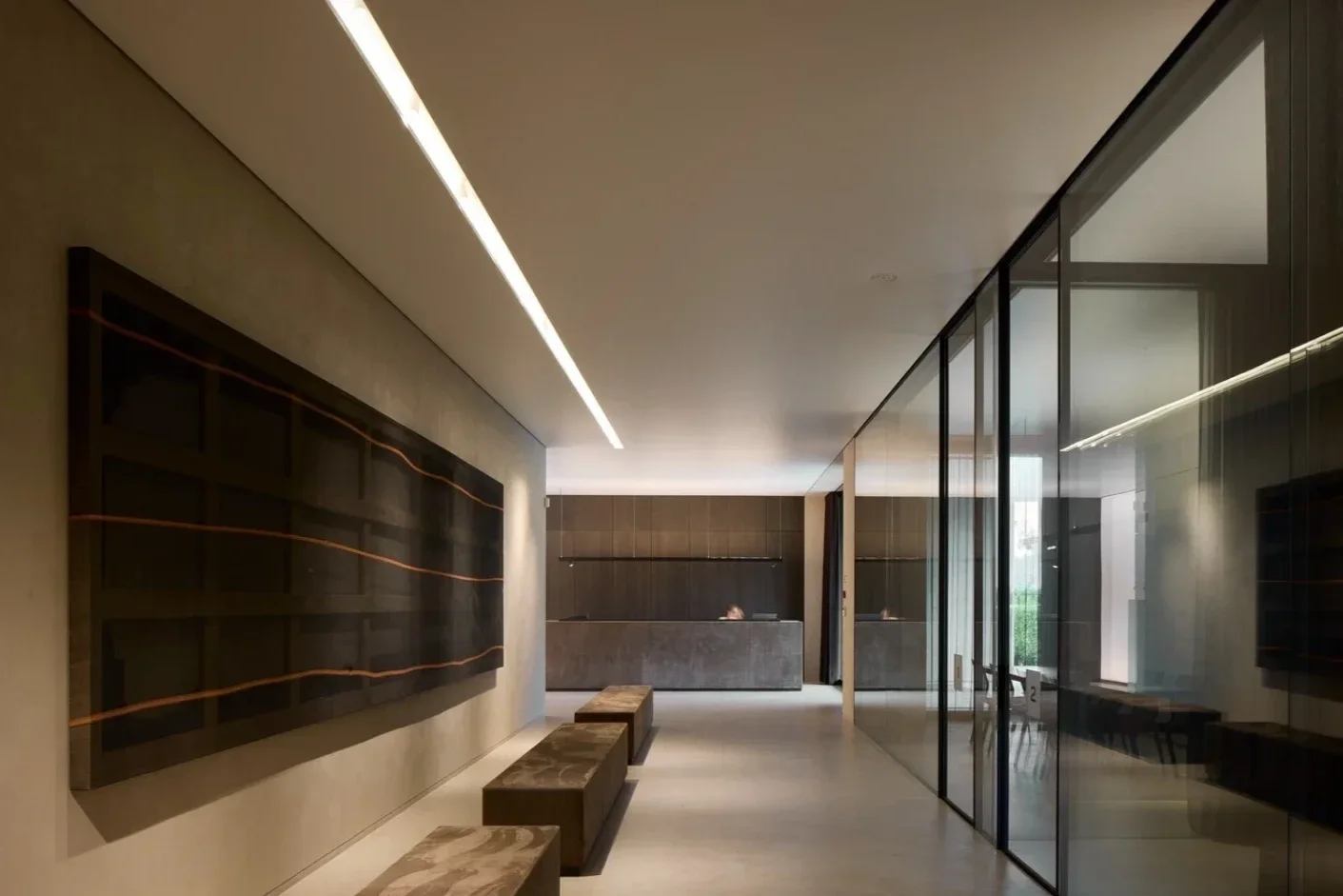 Modern lobby with beige walls, black artwork, bench seating, a reception desk, and glass panels dividing the space.