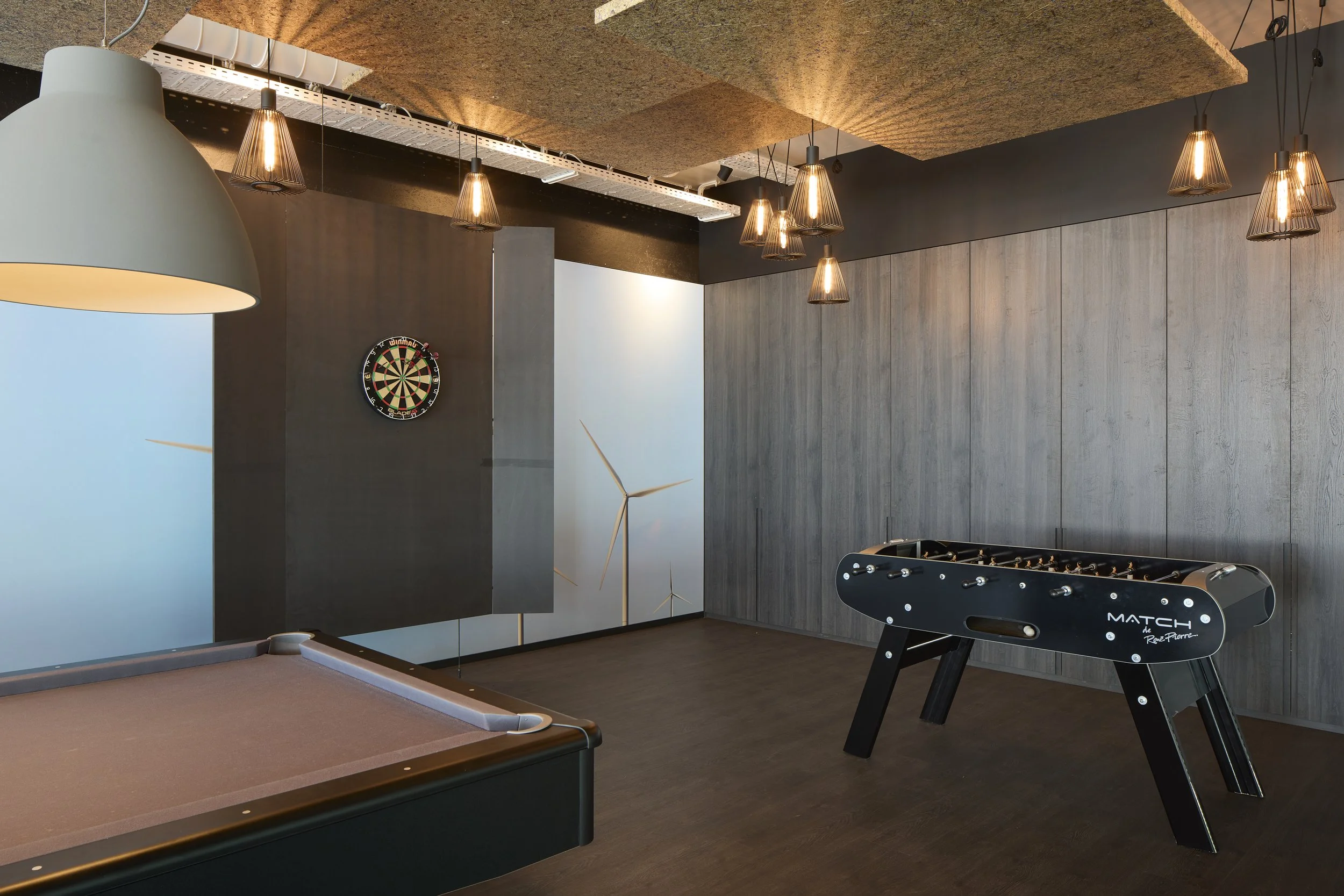 Interior of a game room with a pool table, several pendant lights hanging from the ceiling, a dartboard on the wall, and an air hockey table in the corner.
