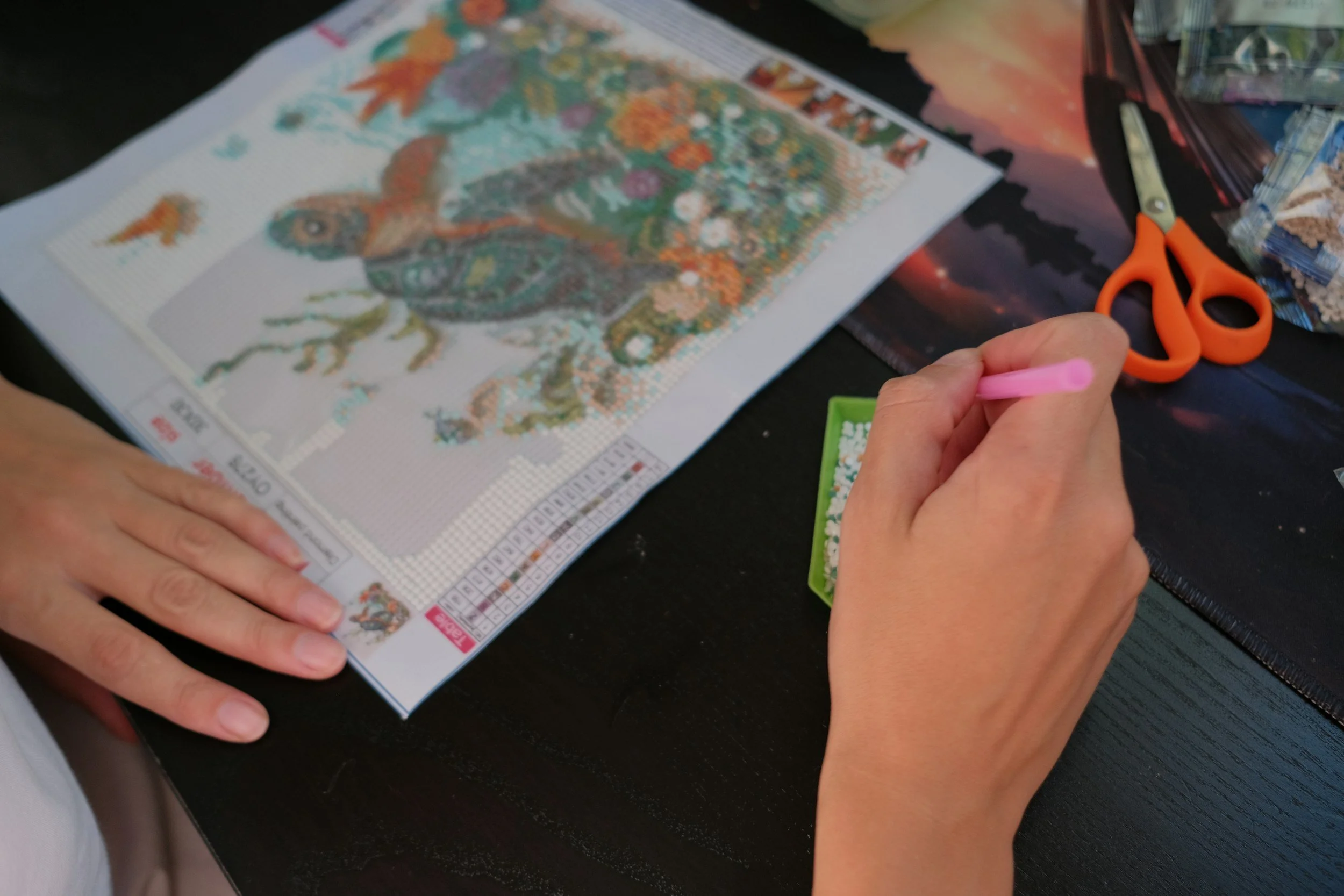 Hands working on a cross-stitch embroidery project featuring a colorful animal design, with scissors and other craft materials nearby.