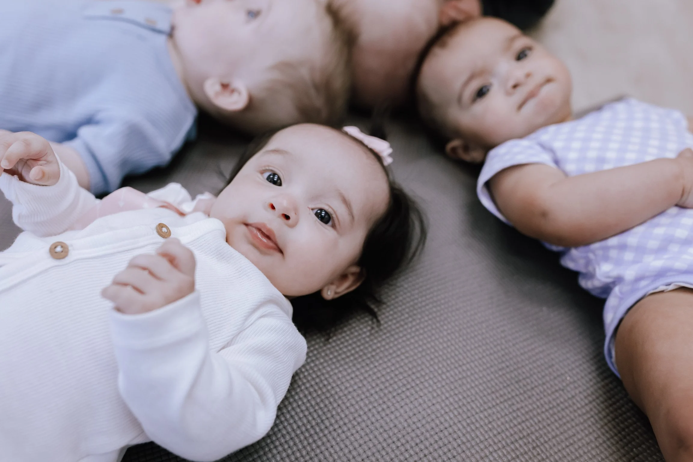 Three young children lying on a mat, looking up, wearing casual clothes.