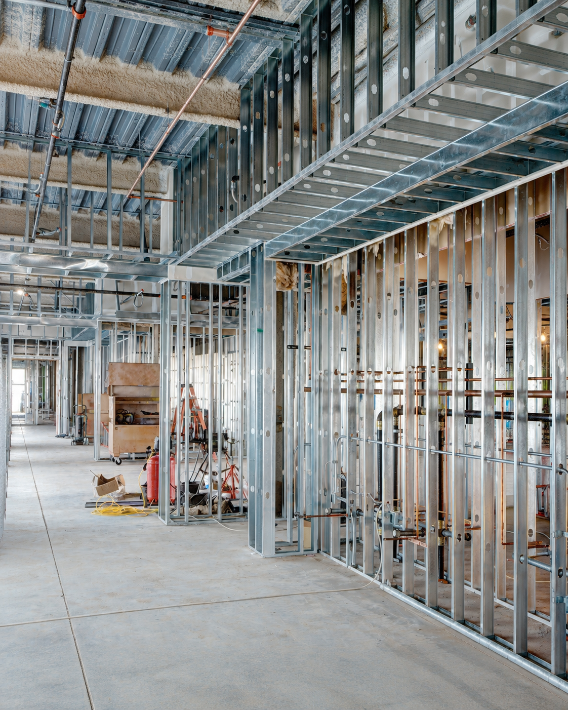 Interior of a building under construction with metal framing, exposed pipes, and construction tools.