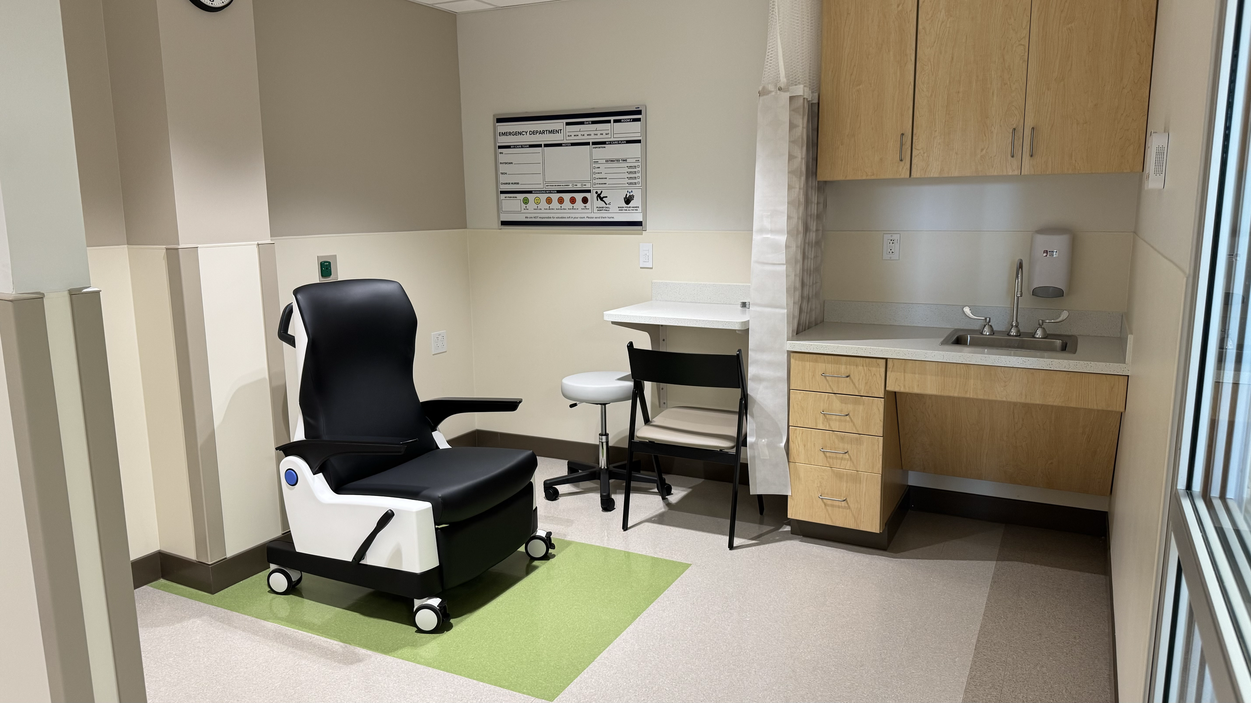 Rivers Health emergency department exam room with medical chair, sink, built-in cabinetry, seating, and clinical equipment.