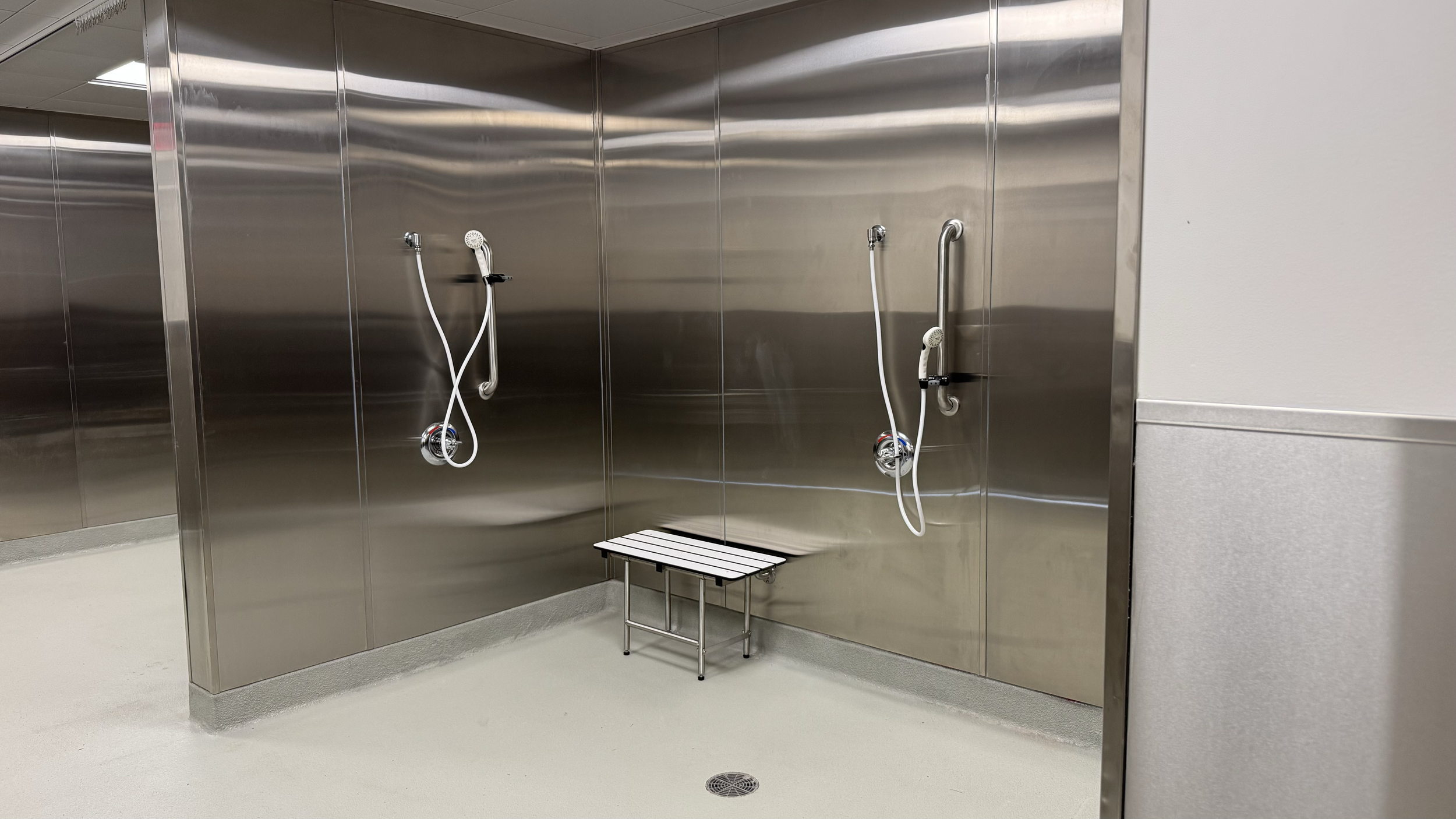 Rivers Health emergency department decontamination shower area with stainless steel fixtures, grab bars, bench, and floor drainage.