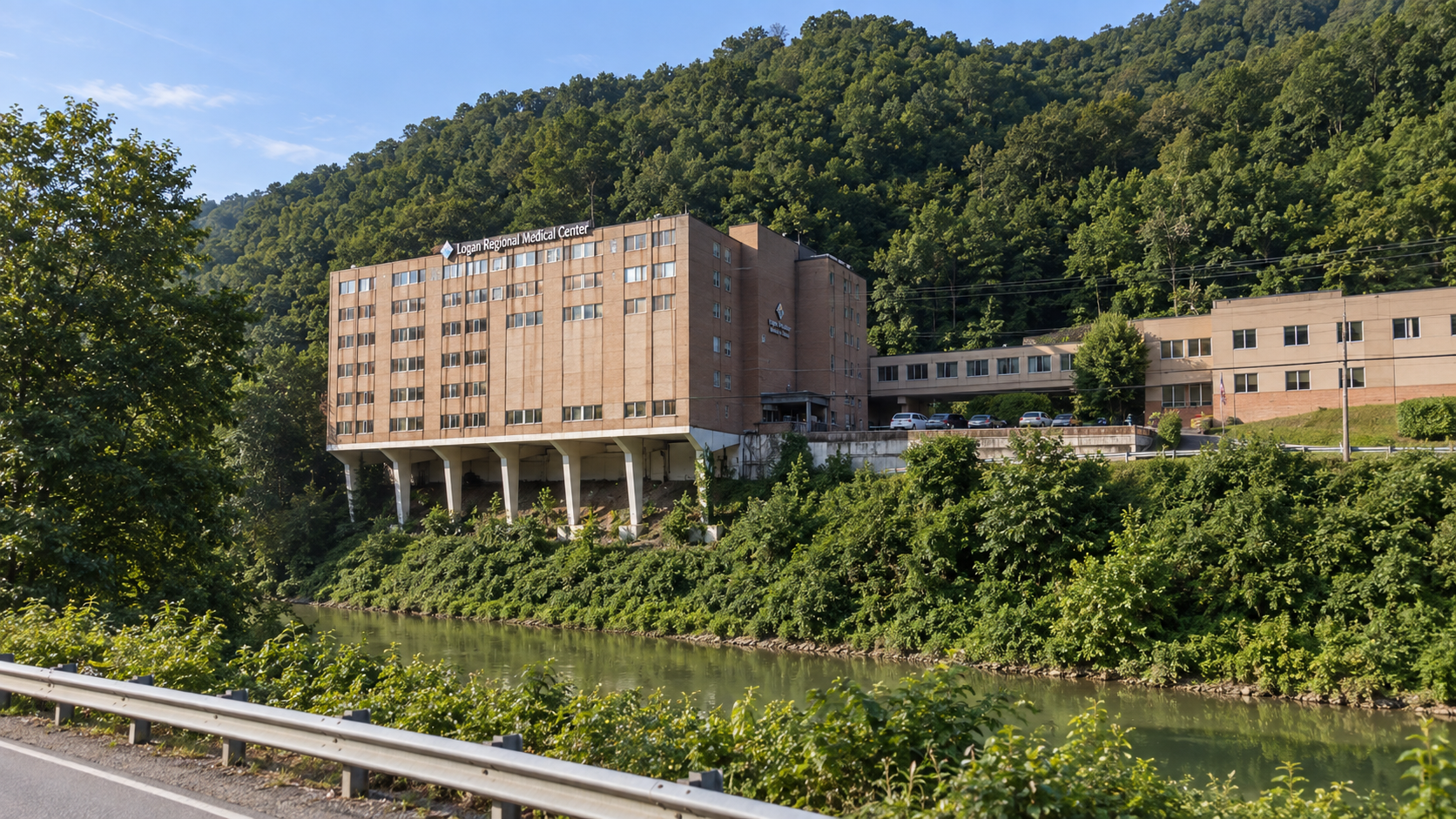 Logan Regional Medical Center building on a hillside with a river in the foreground, surrounded by green trees and hills.