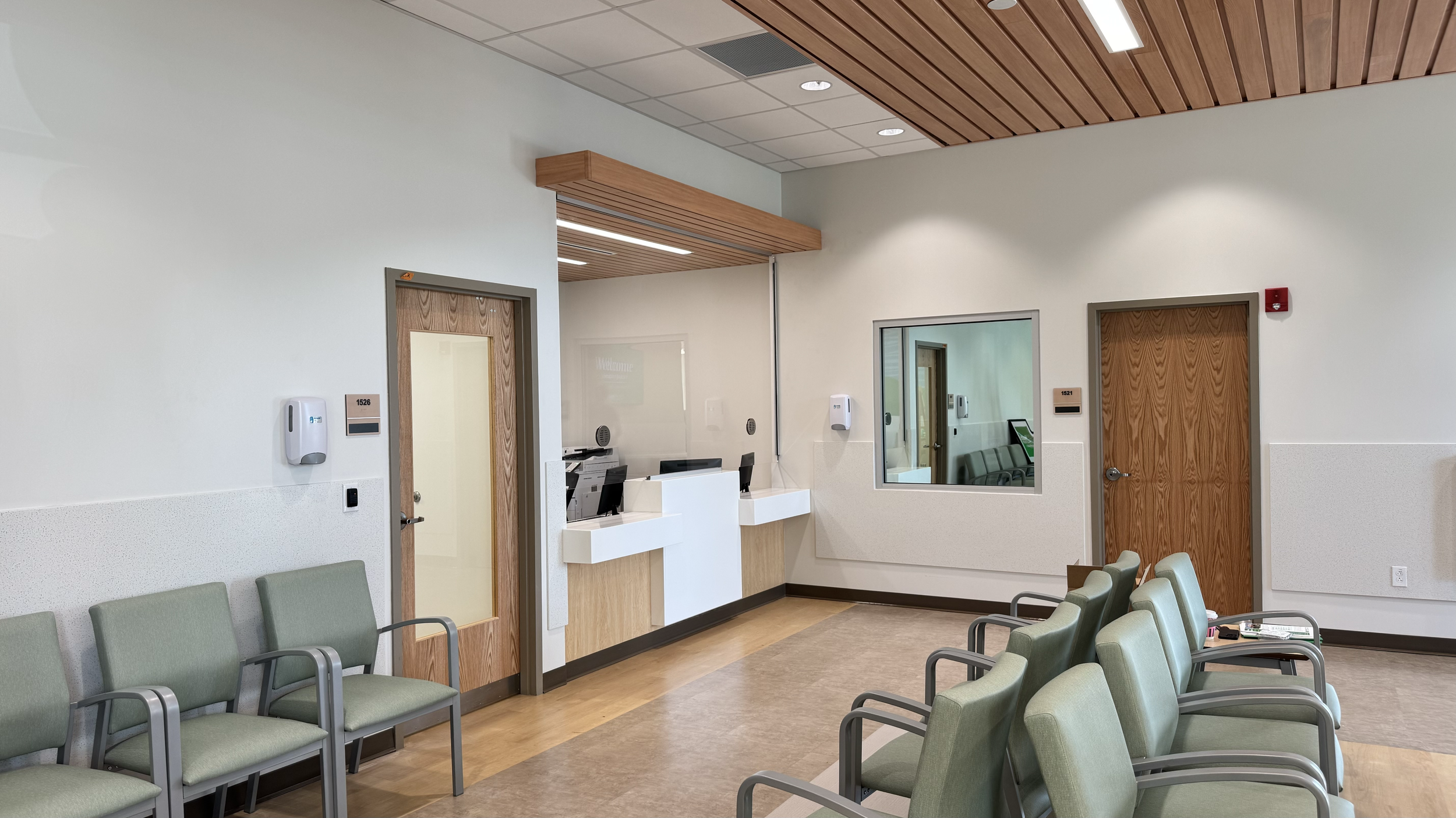 Rivers Health emergency department waiting and registration area with green seating, reception desk, wood accents, and patient access doors.