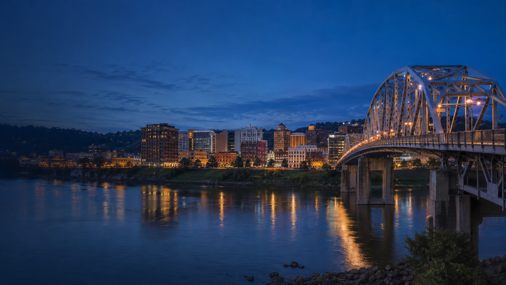 Charleston, West Virginia, skyline at night with an illuminated bridge reflected in the Kanawha River.