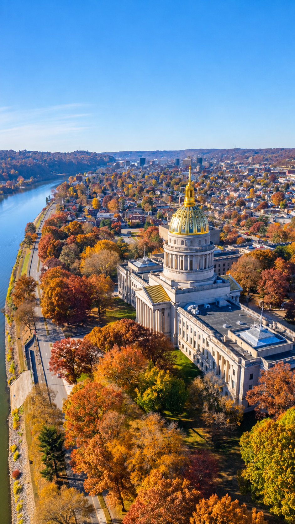 Aerial view of the Tennessee State Capitol building in Nashville, with colorful autumn trees, nearby roads, and the Cumberland River under a clear blue sky.