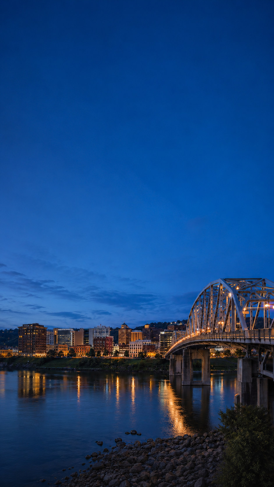 Downtown Charleston, West Virginia, and the Kanawha River at dusk with an illuminated bridge and city skyline.