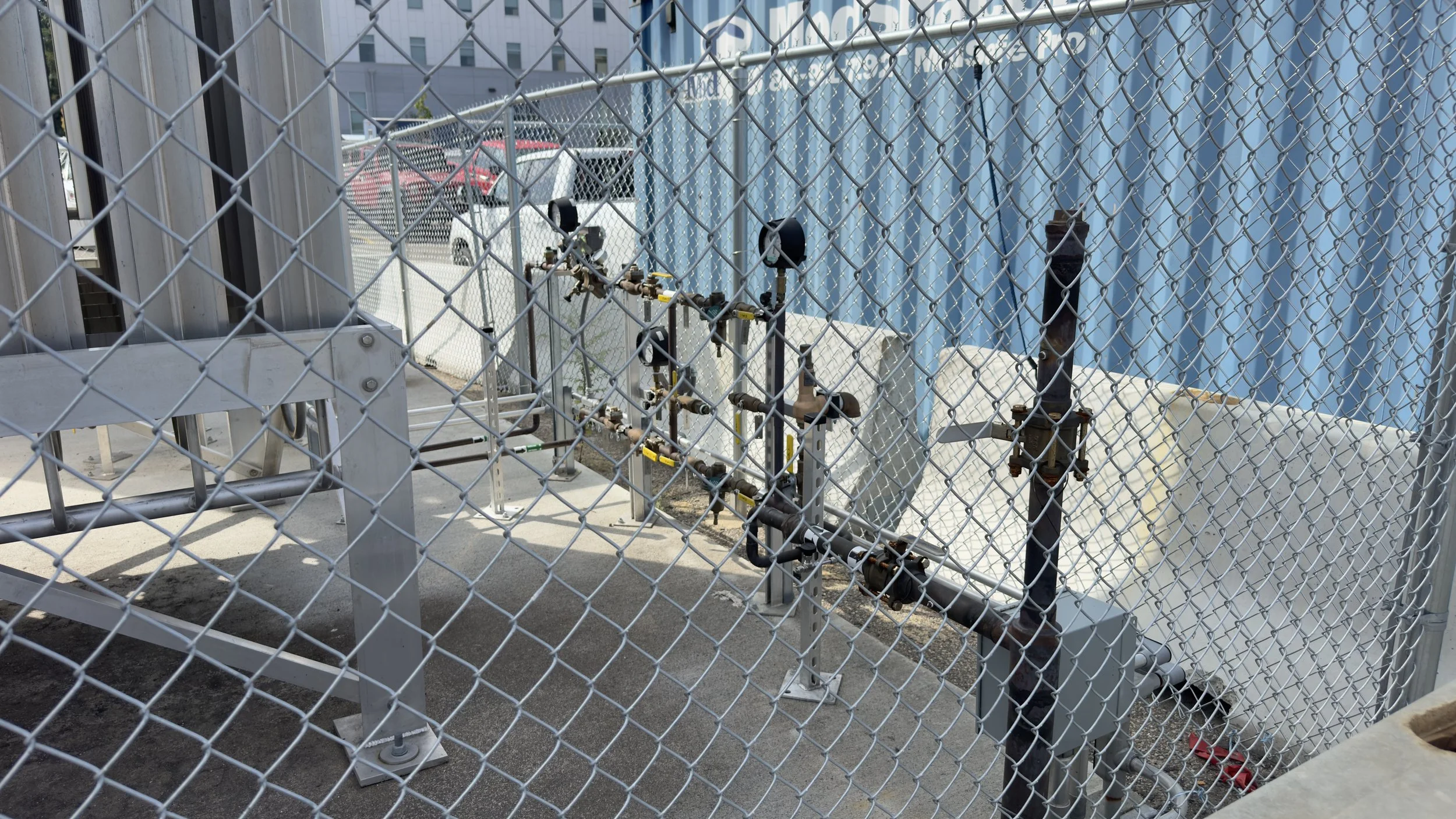 Fenced industrial or utility area with piping, valves, and meters.