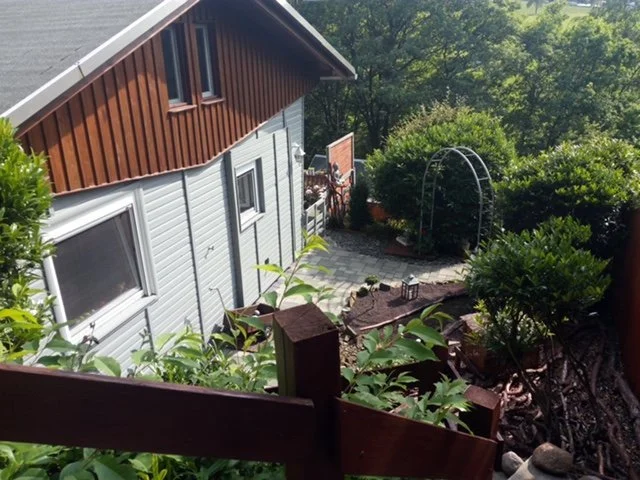 Garten mit Steinsteg, Büschen, und einem Metallbogen, Blick von oben.