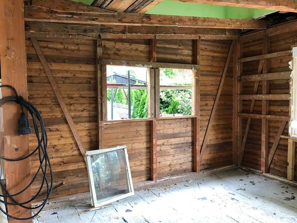 Innenraum eines Holzschuppens oder einer Holzgarage, unmöbliert, mit unvollständigem Fensterrahmen und Wänden, die teilweise noch im Bau sind.