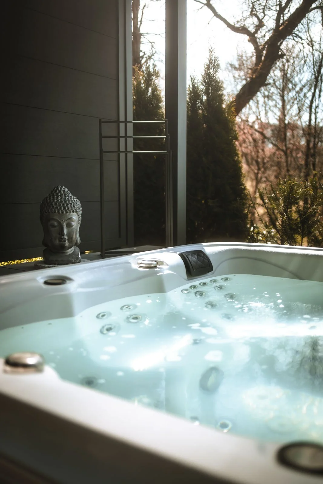 Ein Whirlpool im Freien mit Blick auf Bäume und einen blühenden Kirschbaum. Eine Buddha-Statue befindet sich auf der Kante des Whirlpools.