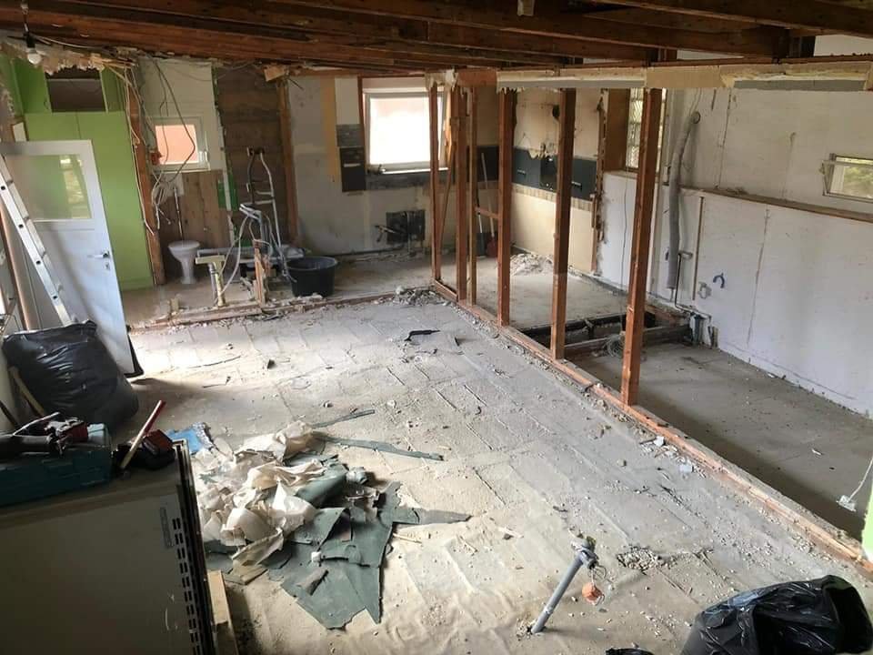 Innenaufnahme einer heruntergerissenen Wand in einem Raum, mit Baustellengeräten und Baumaterialien auf dem Boden.