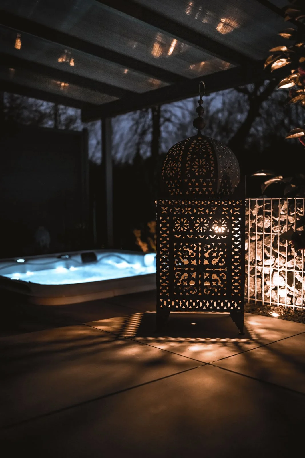 Ein beleuchteter orientalischer Laternen im Außenbereich bei Nacht, in der Nähe eines Hotels mit beheiztem Whirlpool im Hintergrund.
