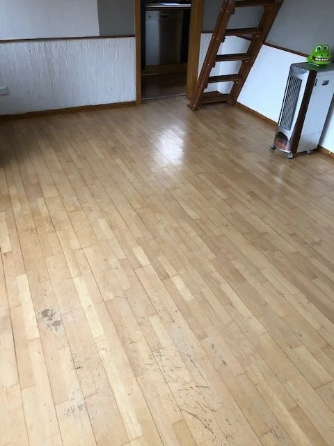 Ein leeres Zimmer mit Holzboden, einer Holztreppe, einem Heizgerät und einem offenen Tür.