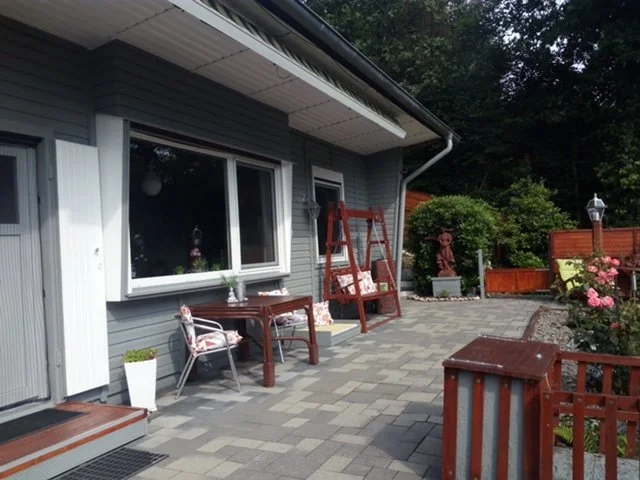 Gartenbereich mit einem Haus im Hintergrund, mehreren Gartenmöbeln, Pflanzen und Dekorationen.