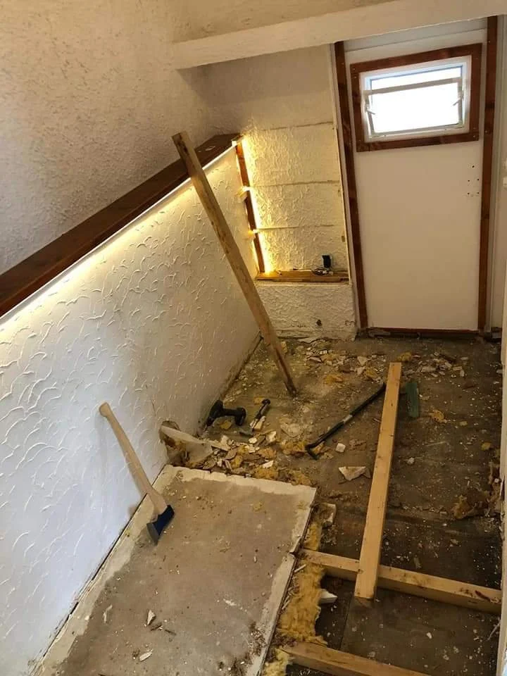 Zimmer im Umbau mit herumliegenden Baustoffen, Werkzeugen und Abbruchresten, Fenster und unvollständigem Boden.