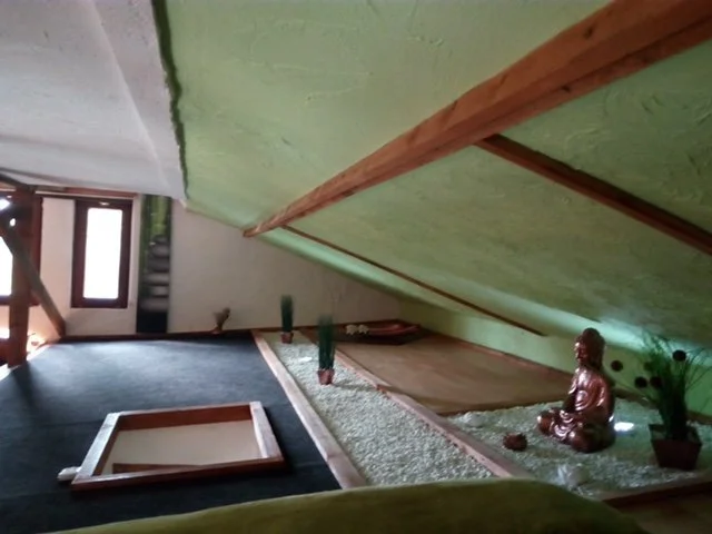 Innenraum eines Dachbodens mit einer kleinen Buddhastatue, Pflanze und Fenstern