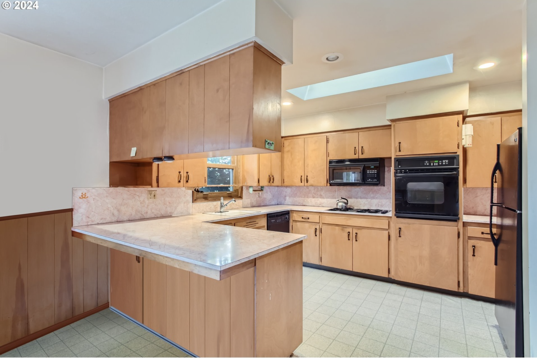 Kitchen with wooden cabinets, marble countertop, black appliances including oven, microwave, and refrigerator, window above sink, and tiled floor.