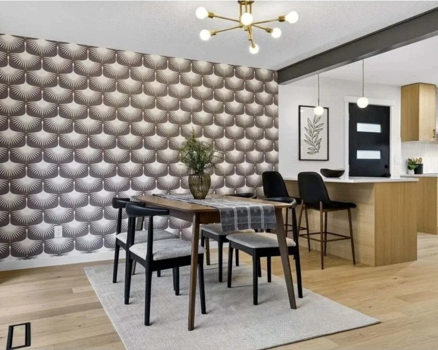 Modern dining area with a patterned wallpaper, wooden table with chairs, a vase with greenery, and a kitchen with barstools and wall art.
