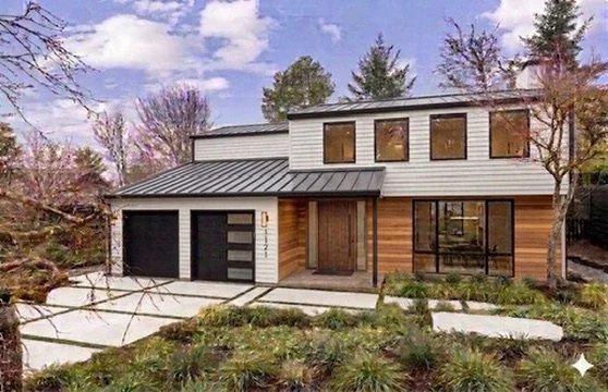 Modern two-story house with a combination of wood and white siding, large front windows, and a concrete driveway with landscaping.