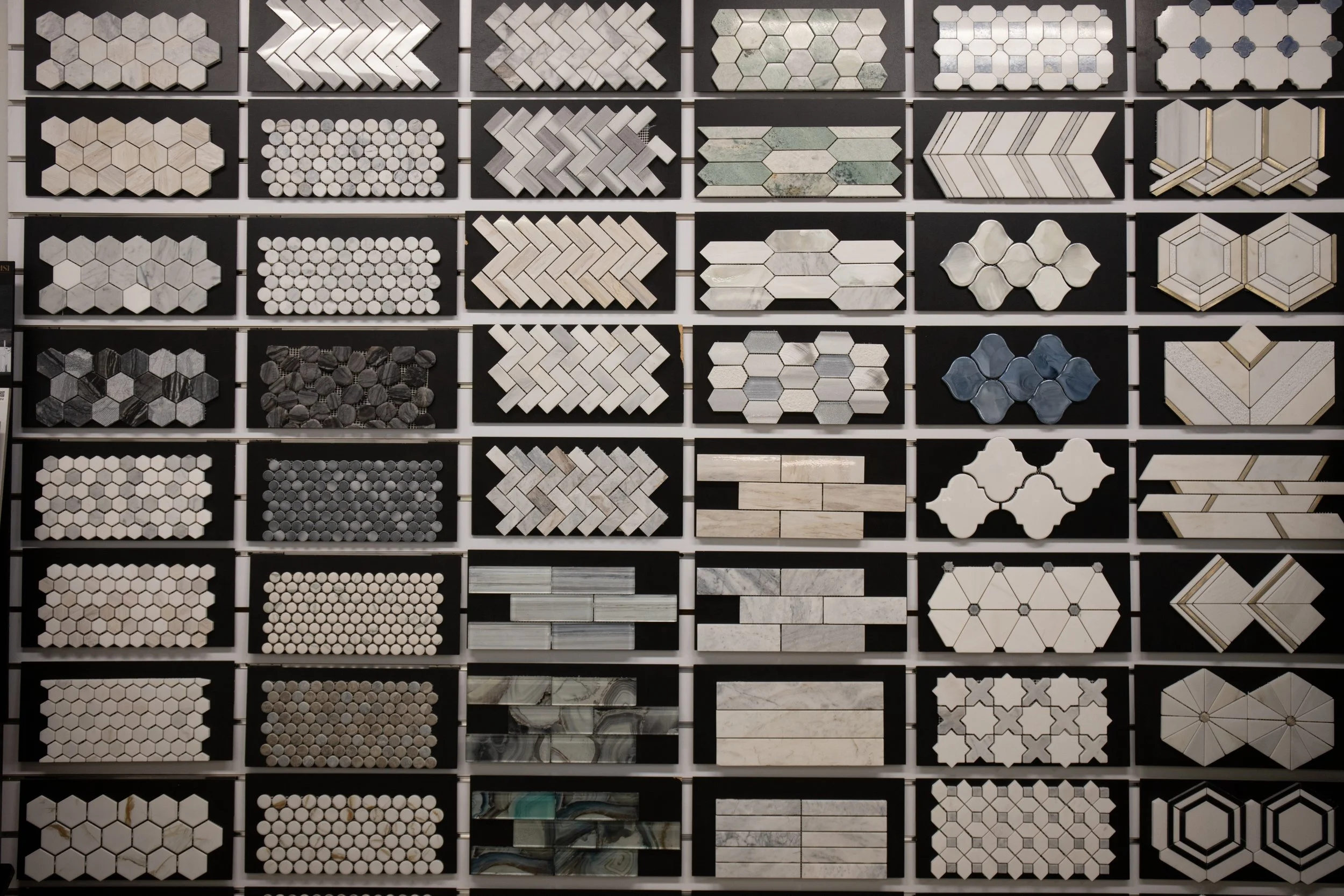A display of various types of tiles arranged in rows, featuring different shapes like hexagons, rectangles, cubes, and other geometric patterns in different colors and materials.