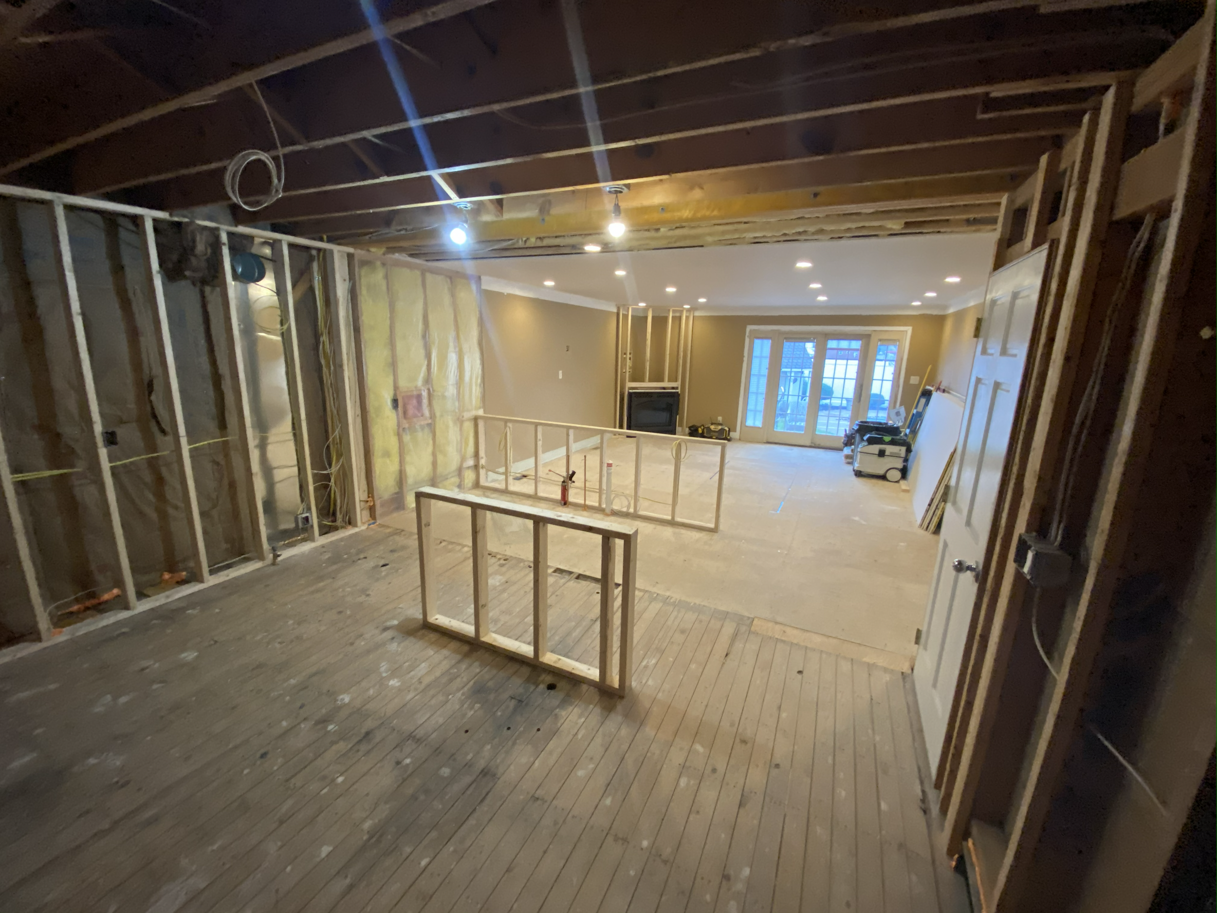 Living room under construction with exposed ceiling beams, unfinished walls, a fireplace, and a view of a large window or sliding door leading outside.