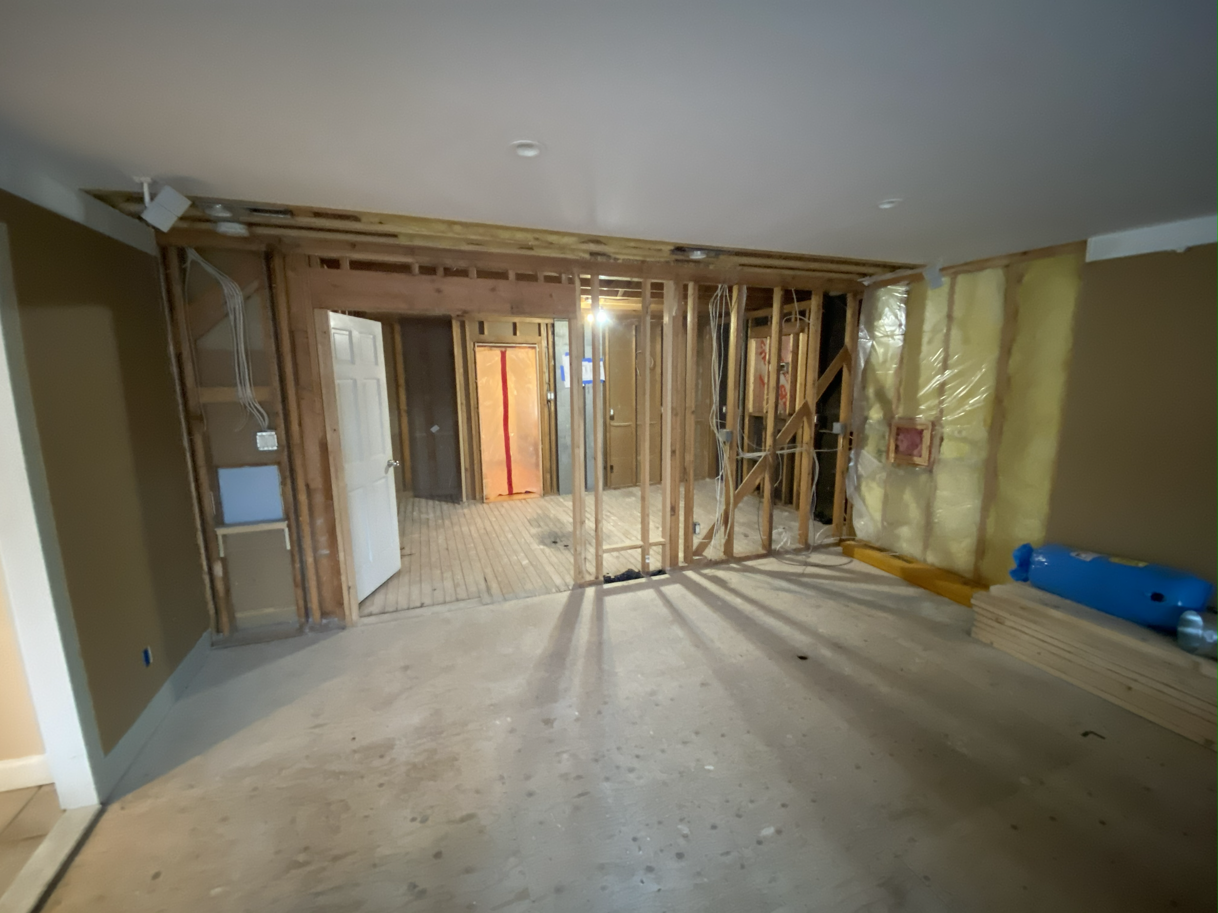 Room under construction with exposed wooden framing, insulation on one wall, and partially finished flooring.