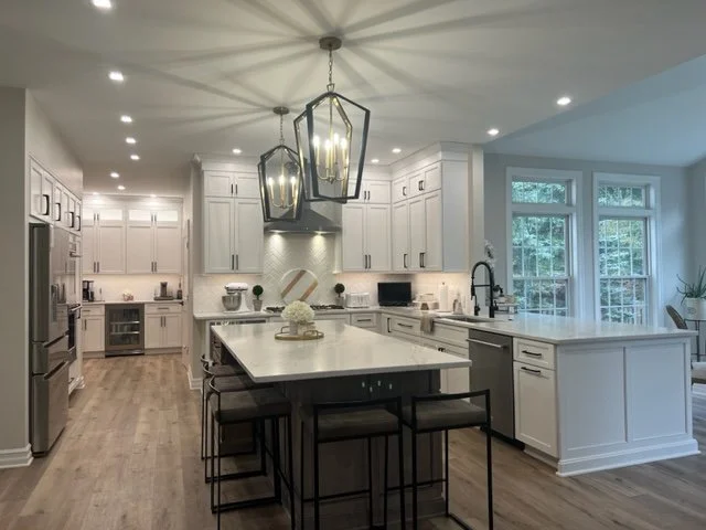 Bright, modern kitchen with white cabinets, a large island with seating, pendant lights, stainless steel appliances, and large windows.