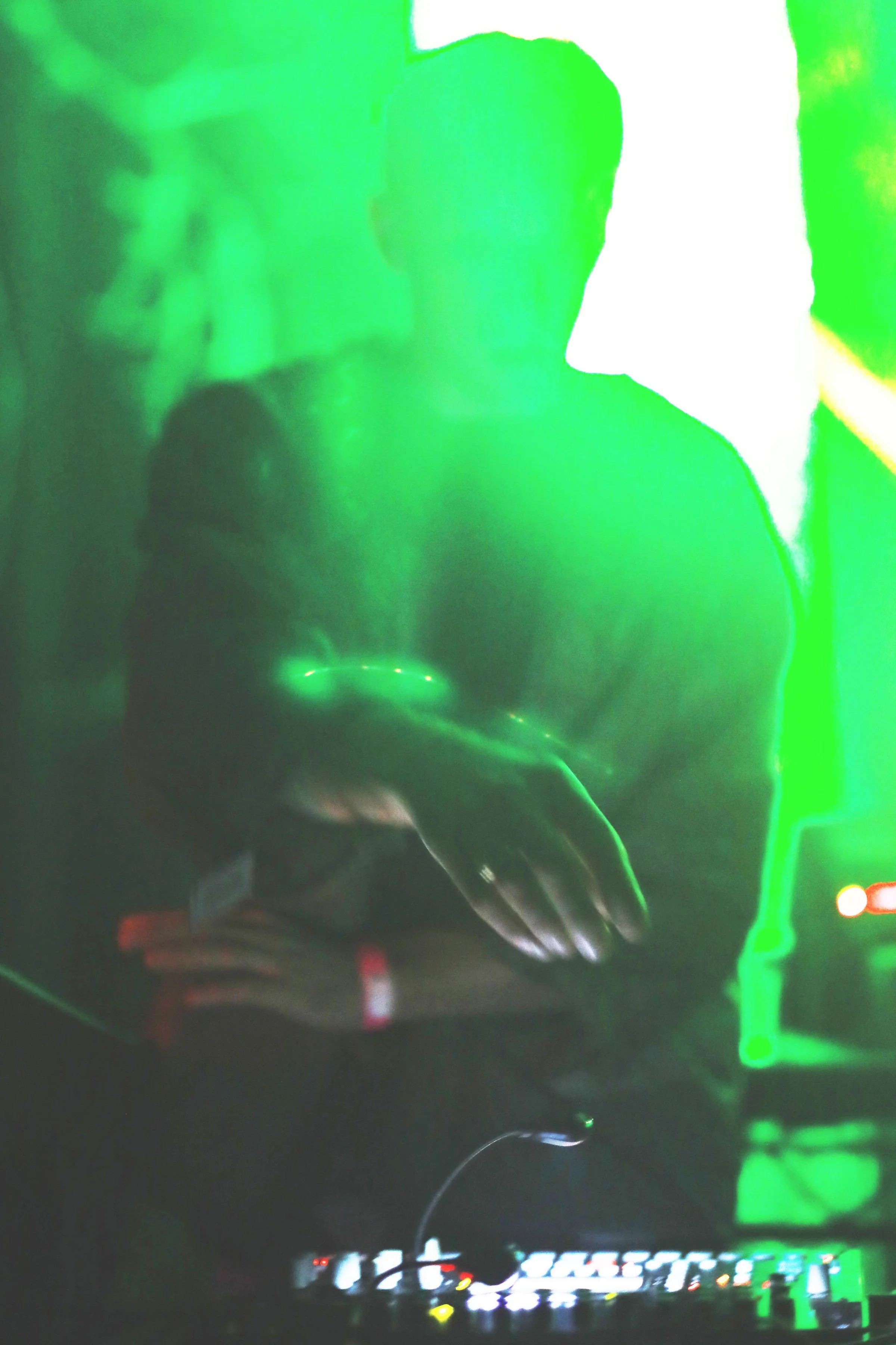 A person with large headphones DJing at a club with green and purple lighting.