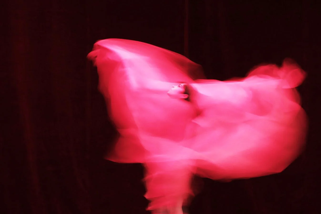 An abstract image of a pink and red flowing form against a black background.