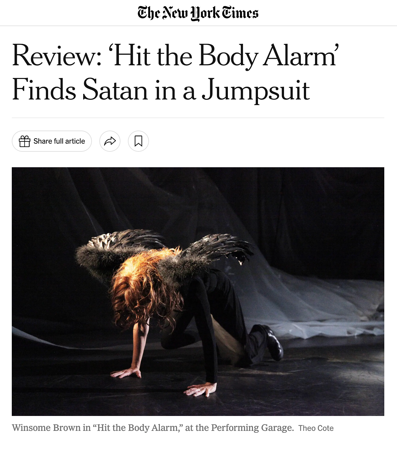 A performer named Winsome Brown on stage at the Performing Garage, dressed in a costume with feathers and black clothing, is kneeling with one hand and one knee on the floor and the other hand supporting her weight, with her head bent down.