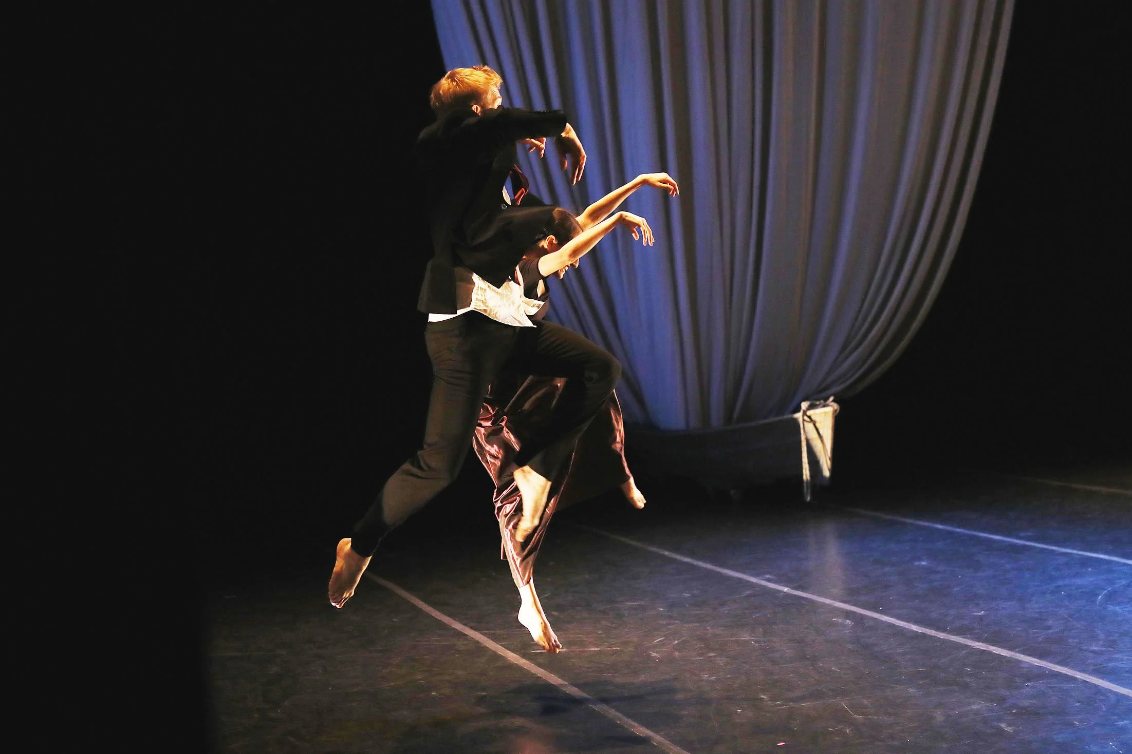 Dancers performing on a stage with a blue curtain in the background.