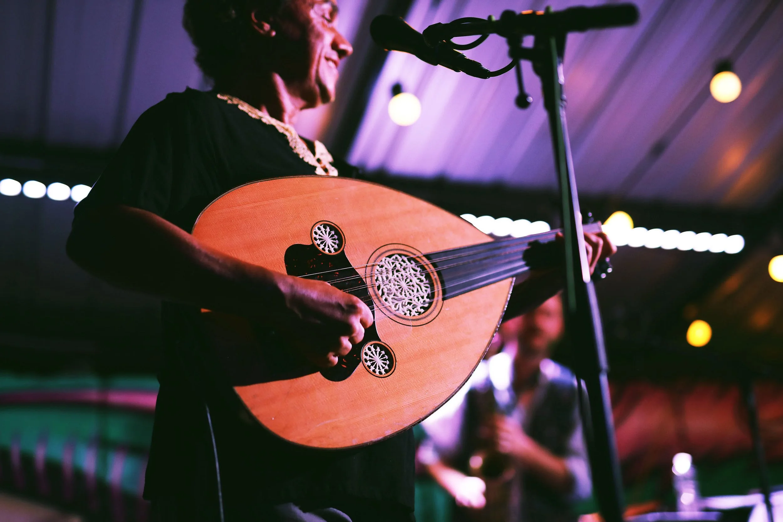 A person playing an acoustic guitar on stage with colorful lights in the background.