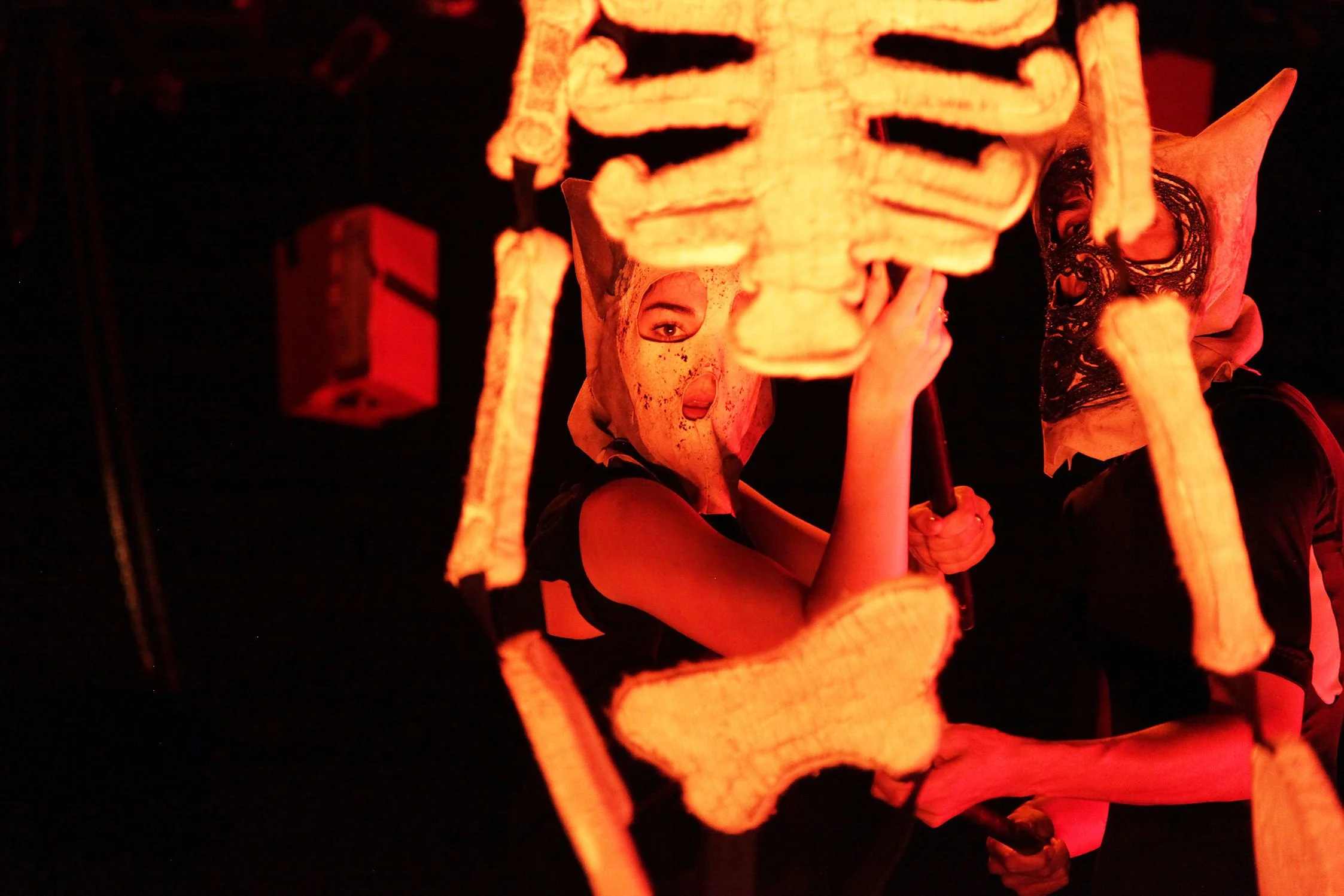 Person wearing a mask with a face design and holding a skull-shaped lantern, illuminated by orange light at night.