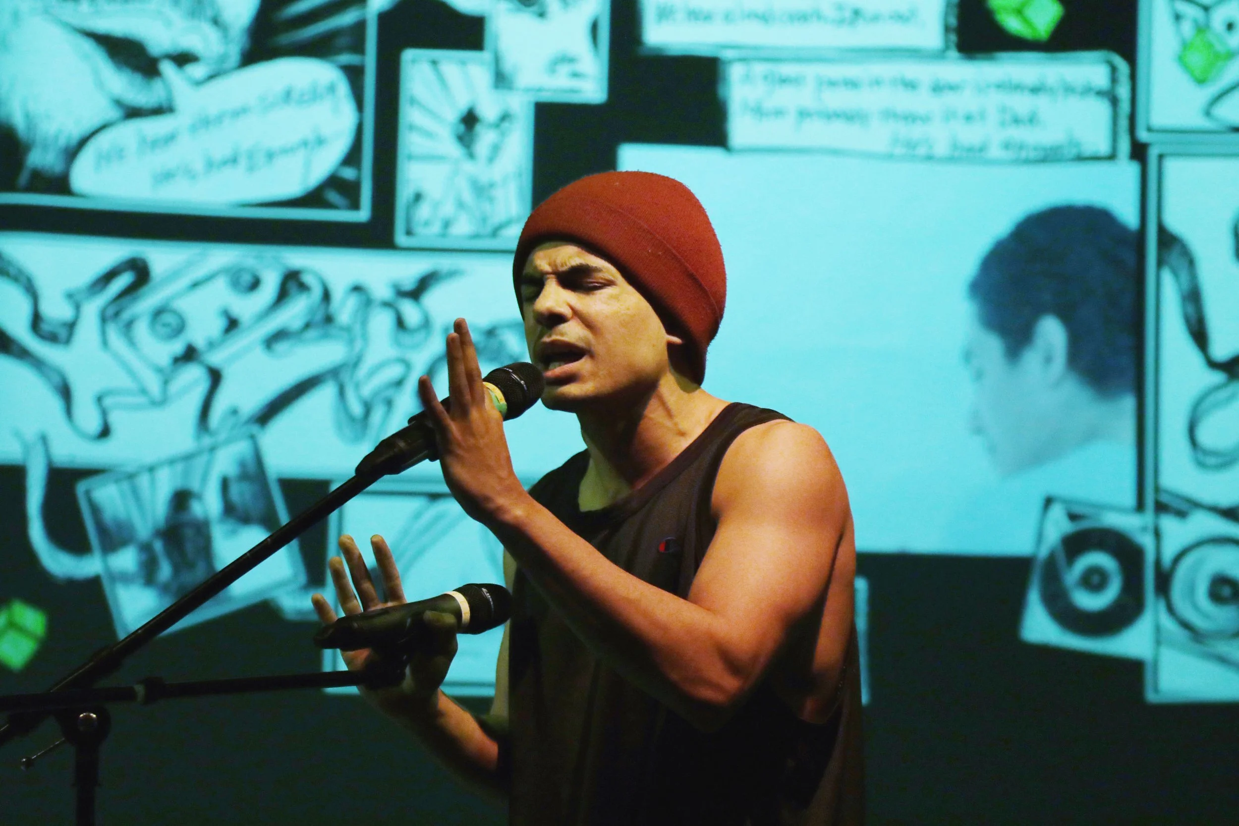 A person wearing a red beanie singing into a microphone, with a blue background featuring comic strip-style illustrations and text.