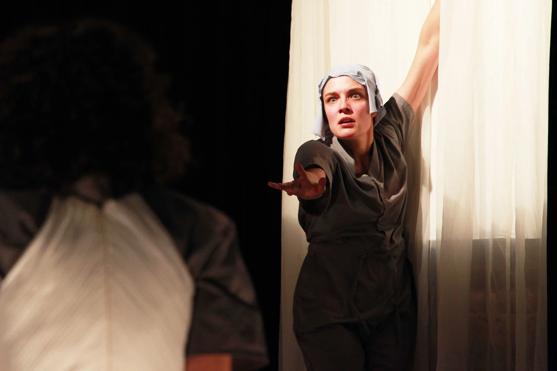 Woman dressed as a maid reaching out with her arm extended and having an intense facial expression, in front of a curtain.