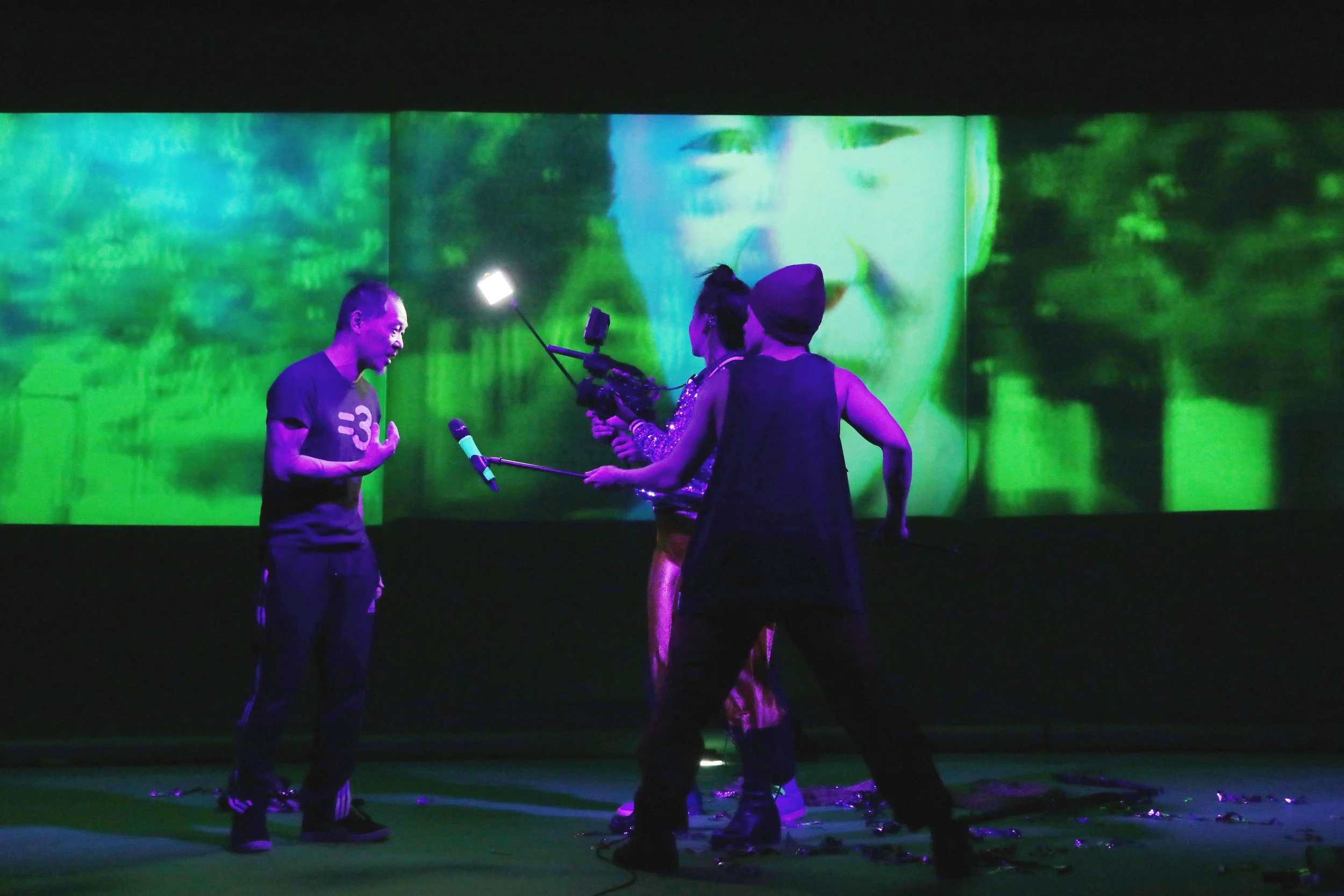 Group of people in a dark room with a large colorful projection of a person's face on the wall behind them.
