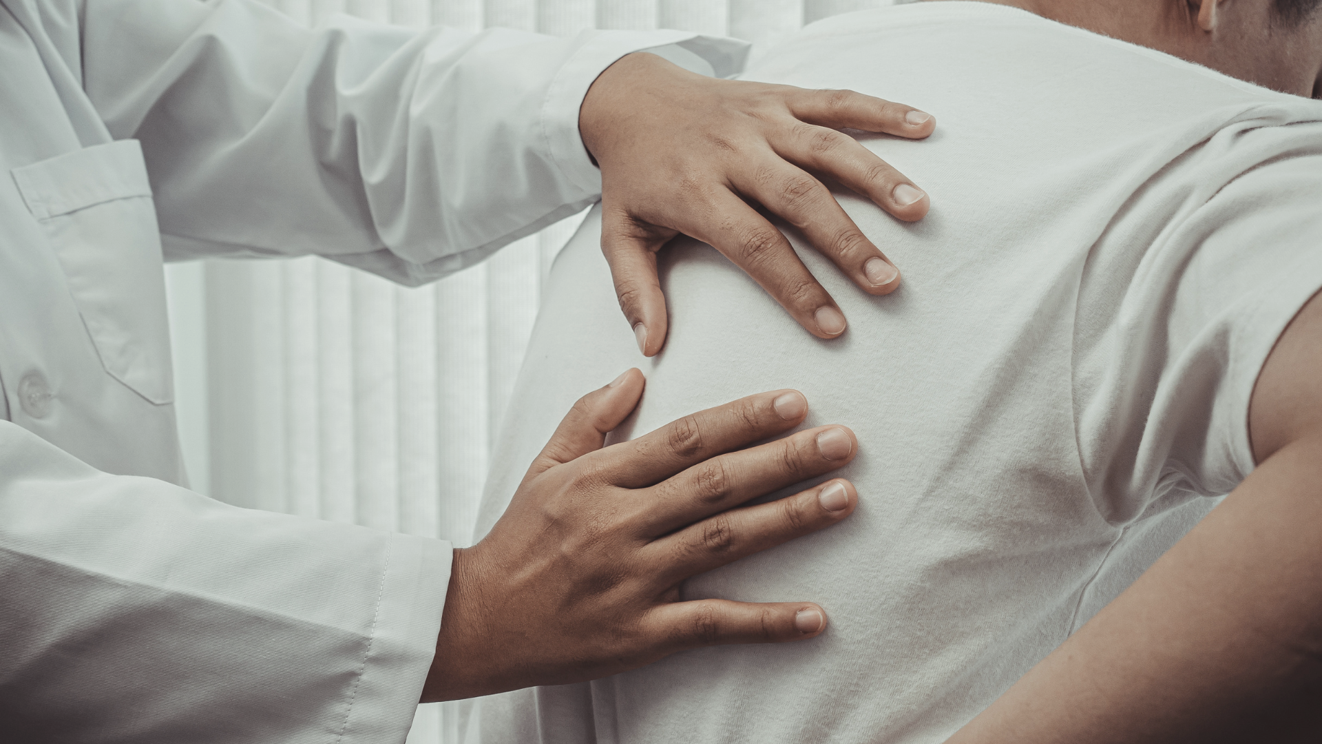 Close-up of a healthcare professional performing a medical examination on a patient's chest with hands placed on the patient's shoulder and side.